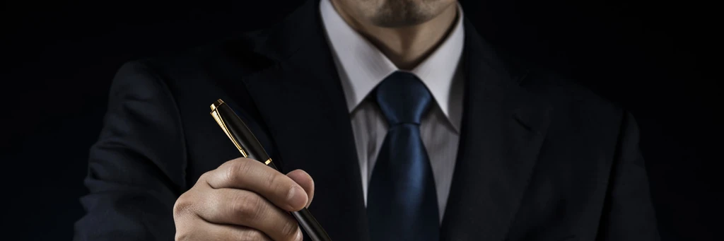 Hand som håller upp exklusiv penna med man i mörk kostym och slips i svart bakgrund