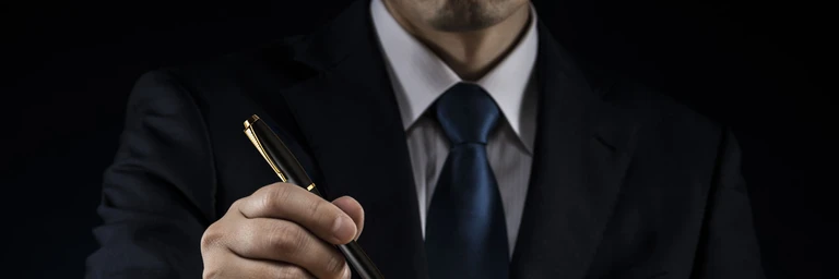 Hand som håller upp exklusiv penna med man i mörk kostym och slips i svart bakgrund
